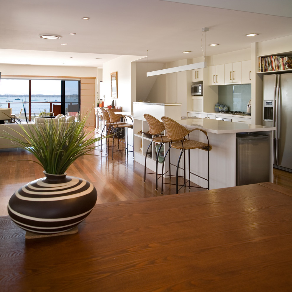 ブリスベンにある高級な広いビーチスタイルのおしゃれなキッチン (ダブルシンク、ガラス板のキッチンパネル、シルバーの調理設備、濃色無垢フローリング) の写真