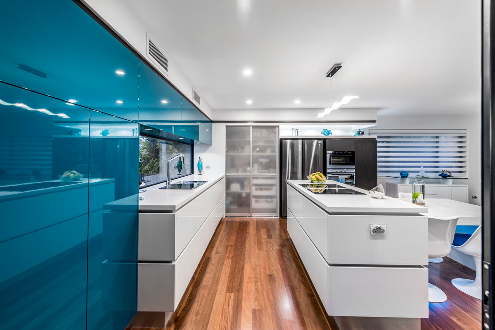 This is an example of a medium sized contemporary l-shaped kitchen pantry in Brisbane with a submerged sink, flat-panel cabinets, turquoise cabinets, engineered stone countertops, black appliances, medium hardwood flooring and an island.