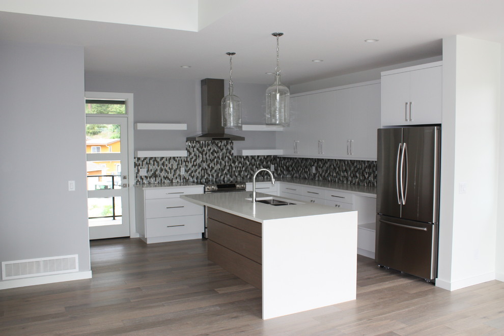 Inspiration for a contemporary u-shaped open plan kitchen in Vancouver with a submerged sink, flat-panel cabinets, white cabinets, engineered stone countertops, glass tiled splashback, stainless steel appliances, light hardwood flooring and an island.