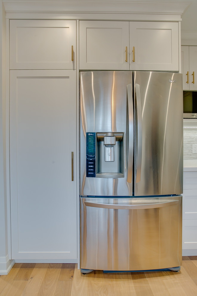 Aménagement d'une cuisine américaine classique en U de taille moyenne avec un évier encastré, un placard à porte shaker, des portes de placard blanches, un plan de travail en quartz modifié, une crédence multicolore, une crédence en carreau de porcelaine, un électroménager en acier inoxydable, un sol en bois brun et un plan de travail blanc.