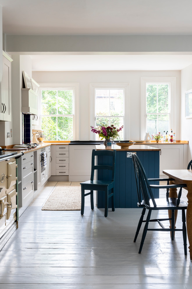 This is an example of a traditional open plan kitchen in London with shaker cabinets, wood worktops and an island.