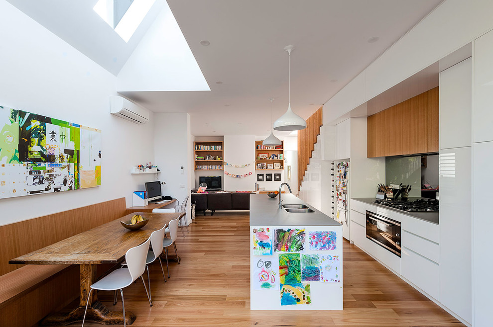 Zweizeilige Moderne Wohnküche mit Doppelwaschbecken, flächenbündigen Schrankfronten, weißen Schränken, braunem Holzboden und Kücheninsel in Melbourne