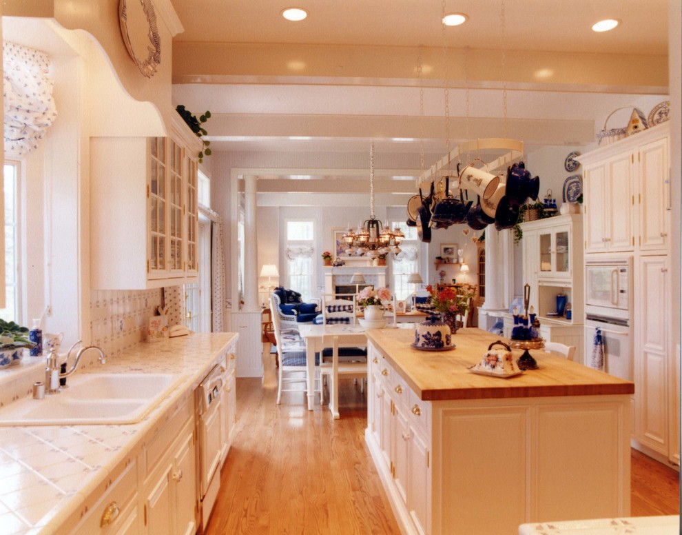 Klassisk inredning av ett stort kök, med en rustik diskho, luckor med upphöjd panel, vita skåp, kaklad bänkskiva, vitt stänkskydd, stänkskydd i keramik, vita vitvaror och mellanmörkt trägolv