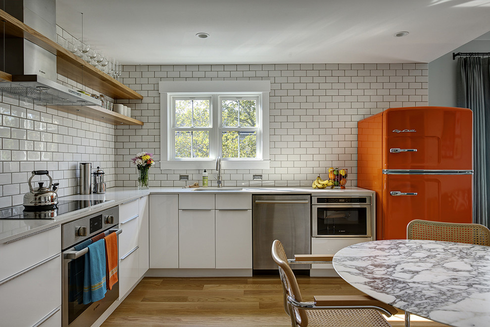 На фото: угловая кухня в современном стиле с обеденным столом, одинарной мойкой, плоскими фасадами, белыми фасадами, белым фартуком, фартуком из плитки кабанчик, цветной техникой, светлым паркетным полом и мойкой у окна с