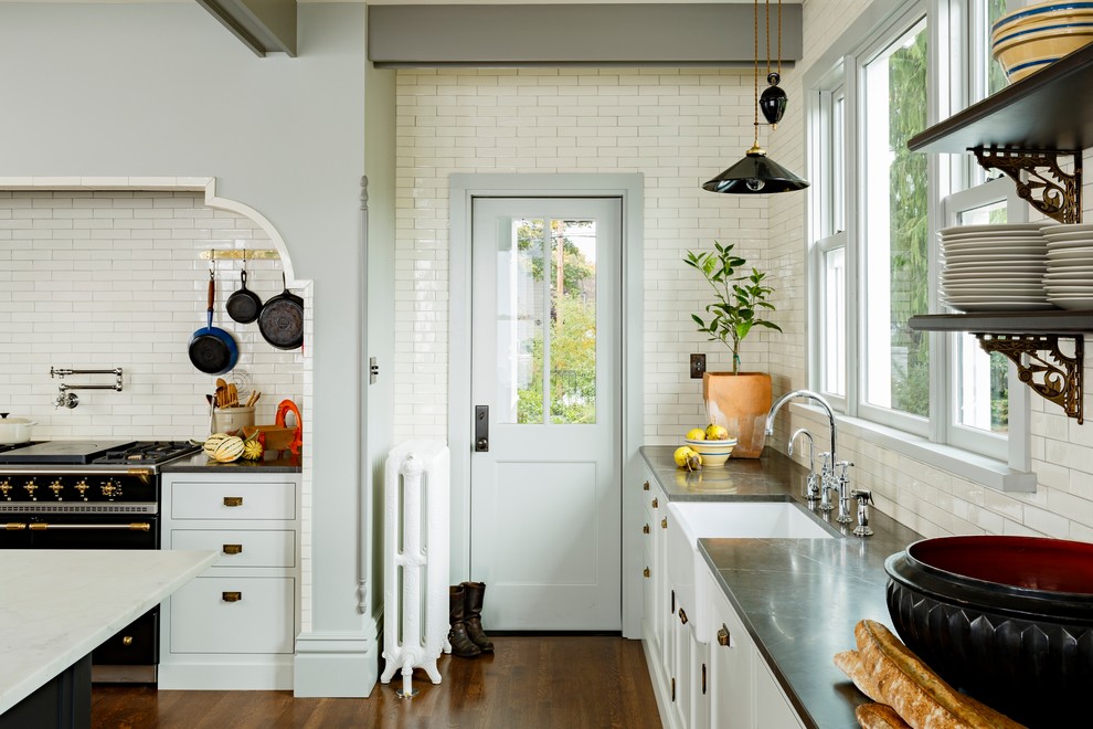 Foto på ett stort lantligt kök, med en rustik diskho, släta luckor, vita skåp, marmorbänkskiva, vitt stänkskydd, stänkskydd i tunnelbanekakel, svarta vitvaror, mörkt trägolv och en köksö