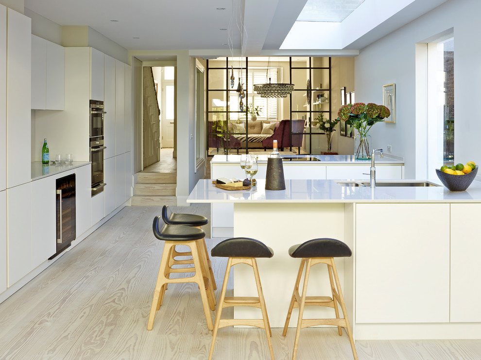 Moderne Küche mit Doppelwaschbecken, flächenbündigen Schrankfronten, weißen Schränken, hellem Holzboden, Halbinsel und beigem Boden in Sonstige