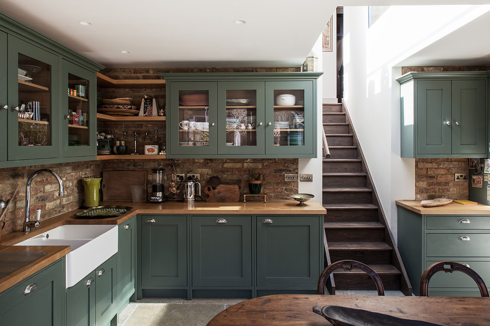 Eat-in kitchen - transitional l-shaped eat-in kitchen idea in London with glass-front cabinets, green cabinets, wood countertops, no island and a farmhouse sink
