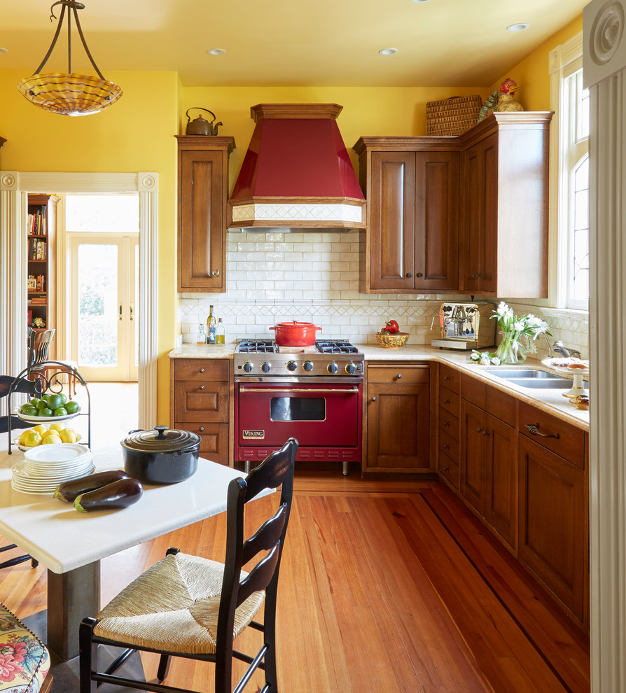 Mid-sized ornate l-shaped medium tone wood floor and brown floor enclosed kitchen photo in San Francisco with a double-bowl sink, raised-panel cabinets, dark wood cabinets, marble countertops, white backsplash, ceramic backsplash, colored appliances and no island