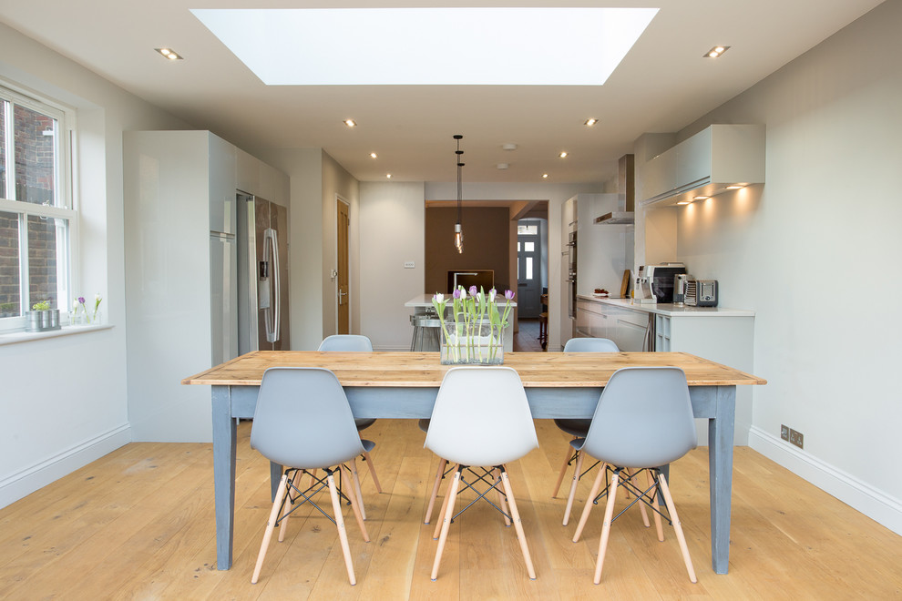 Zweizeilige Moderne Wohnküche mit flächenbündigen Schrankfronten, grauen Schränken, Küchengeräten aus Edelstahl, hellem Holzboden, Kücheninsel, integriertem Waschbecken, Mineralwerkstoff-Arbeitsplatte, Küchenrückwand in Grau und Glasrückwand in Surrey