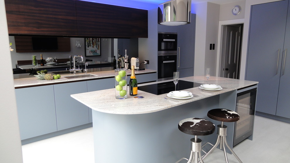 Photo of a medium sized contemporary l-shaped kitchen/diner in London with an integrated sink, flat-panel cabinets, blue cabinets, granite worktops, grey splashback, glass sheet splashback, integrated appliances, porcelain flooring and an island.