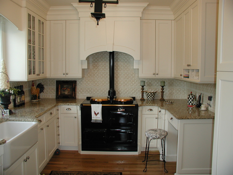 Inspiration for a mid-sized timeless u-shaped medium tone wood floor eat-in kitchen remodel in Cleveland with a farmhouse sink, recessed-panel cabinets, white cabinets, granite countertops, white backsplash, ceramic backsplash and black appliances