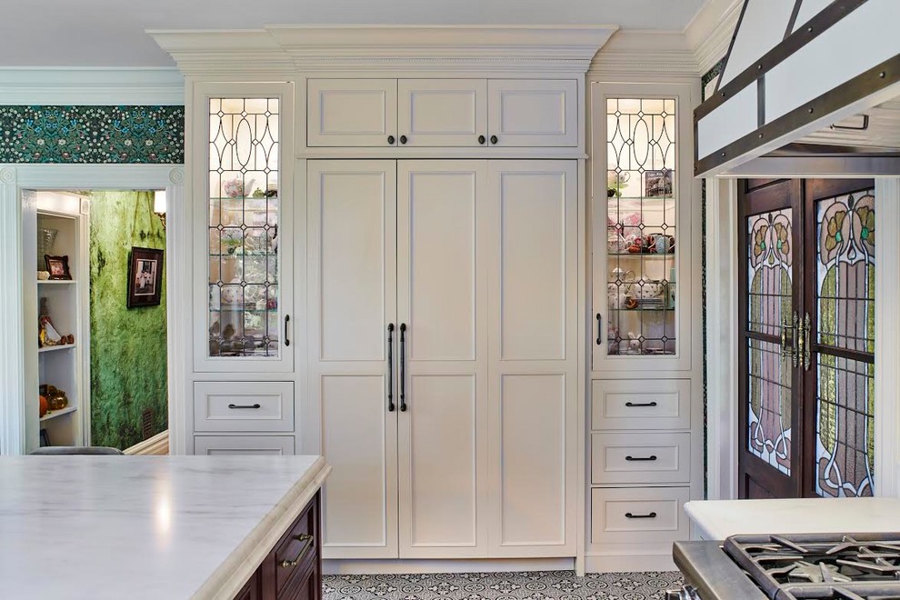 Klassisk inredning av ett avskilt vit vitt u-kök, med en rustik diskho, luckor med profilerade fronter, vita skåp, marmorbänkskiva, vitt stänkskydd, integrerade vitvaror, klinkergolv i keramik, en köksö och flerfärgat golv