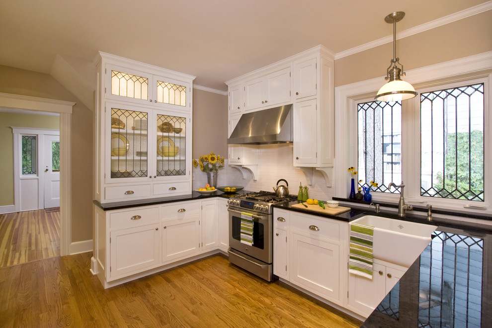 Enclosed kitchen - small traditional u-shaped light wood floor enclosed kitchen idea in New York with a farmhouse sink, beaded inset cabinets, white cabinets, laminate countertops, white backsplash, ceramic backsplash, stainless steel appliances and a peninsula