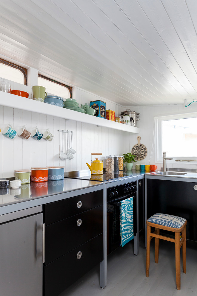 Ejemplo de cocinas en L escandinava con armarios con paneles lisos, puertas de armario negras y electrodomésticos de acero inoxidable