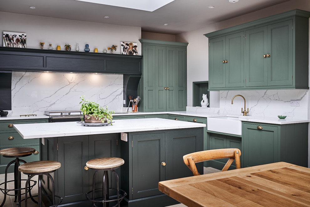 Classic l-shaped kitchen/diner in Other with a belfast sink, shaker cabinets, green cabinets, white splashback, stone slab splashback, an island and white worktops.