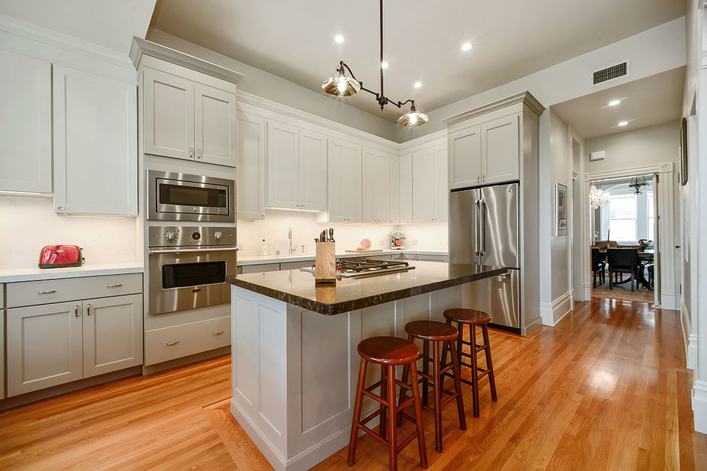 Inredning av ett klassiskt mellanstort kök, med en undermonterad diskho, vita skåp, bänkskiva i kvarts, vitt stänkskydd, rostfria vitvaror, mellanmörkt trägolv, en köksö, luckor med infälld panel och brunt golv
