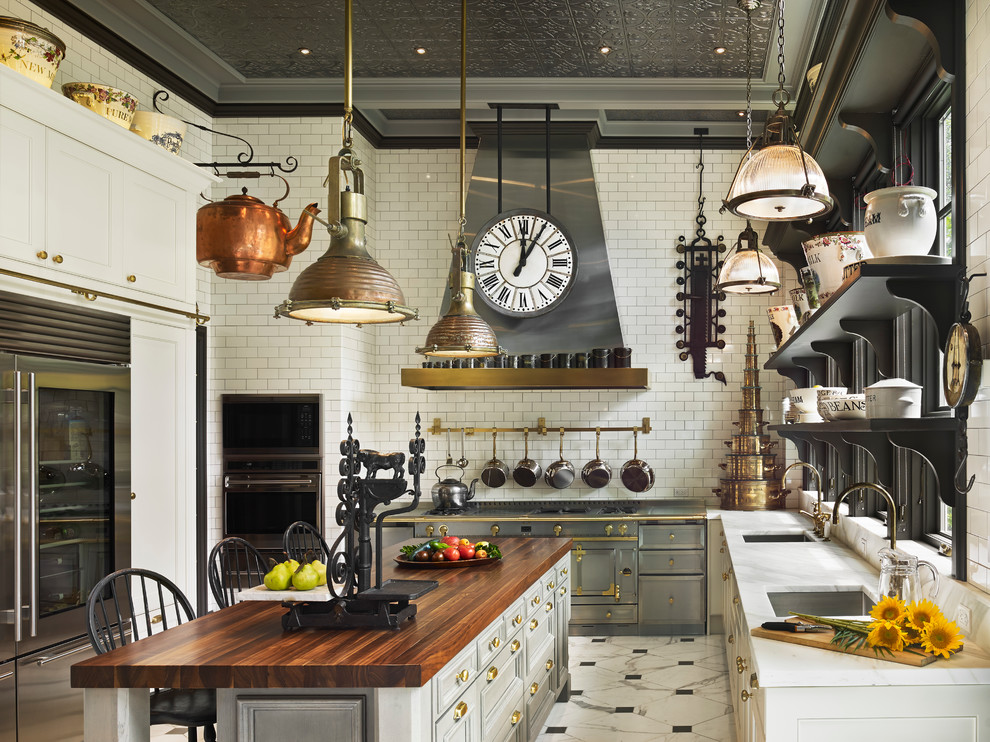 Bild på ett stort vintage kök, med en undermonterad diskho, vita skåp, träbänkskiva, vitt stänkskydd, stänkskydd i tunnelbanekakel, rostfria vitvaror, marmorgolv, en köksö och luckor med infälld panel