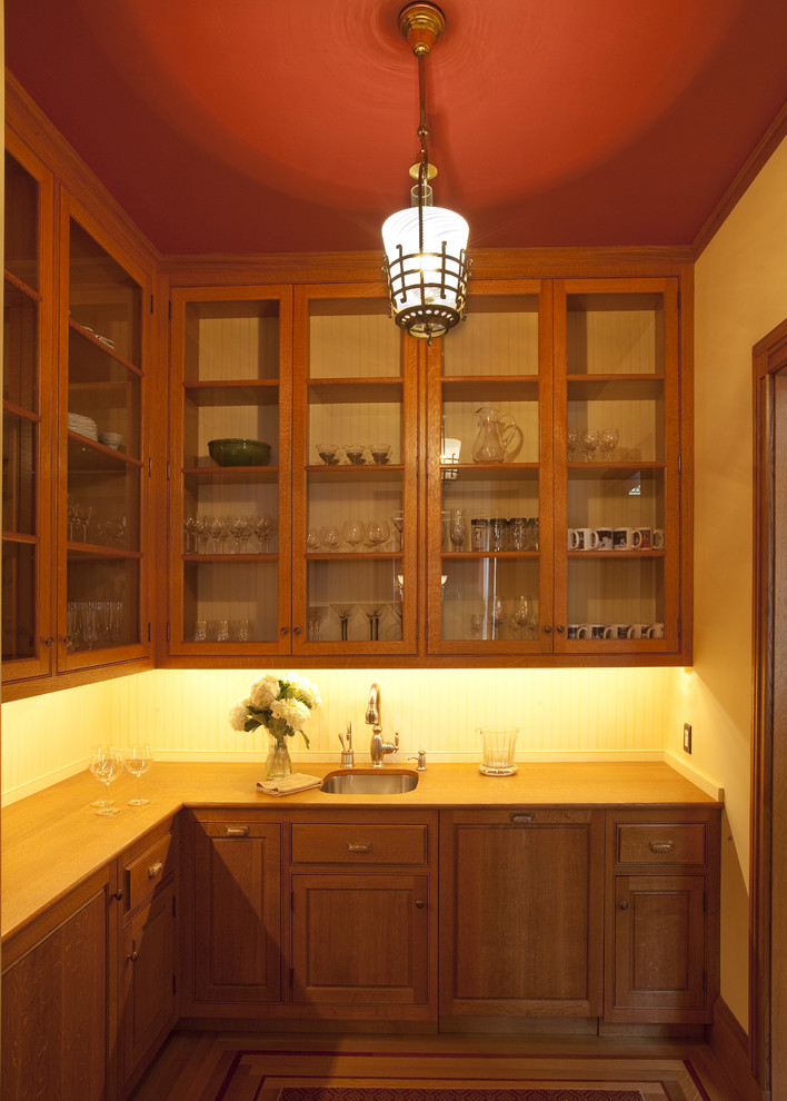 На фото: угловая кухня в викторианском стиле с врезной мойкой, стеклянными фасадами, фасадами цвета дерева среднего тона и деревянной столешницей с