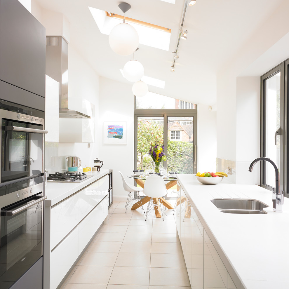 На фото: параллельная кухня в современном стиле с обеденным столом, врезной мойкой, плоскими фасадами, белыми фасадами и белым фартуком с