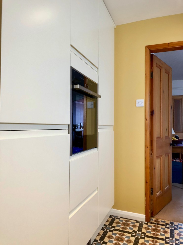 This is an example of a medium sized classic galley enclosed kitchen in Other with a submerged sink, flat-panel cabinets, beige cabinets, composite countertops, blue splashback, ceramic splashback, stainless steel appliances, ceramic flooring, no island, multi-coloured floors and beige worktops.