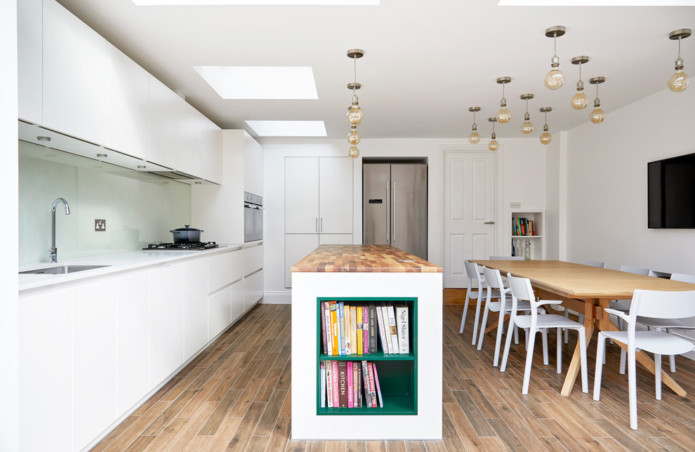 Bild på ett funkis vit vitt l-kök, med en undermonterad diskho, släta luckor, vita skåp, en köksö och brunt golv