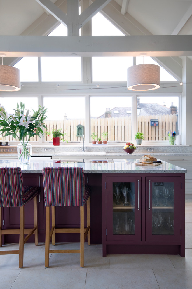 Cette image montre une cuisine parallèle rustique avec un évier posé, un placard à porte vitrée, des portes de placard violettes, une crédence grise, îlot, un sol beige et fenêtre au-dessus de l'évier.