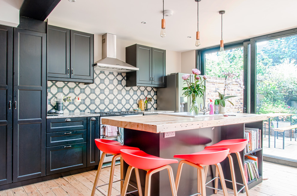 Moderne Küche mit Schrankfronten mit vertiefter Füllung, schwarzen Schränken, bunter Rückwand, Küchengeräten aus Edelstahl, hellem Holzboden, Kücheninsel und braunem Boden in London