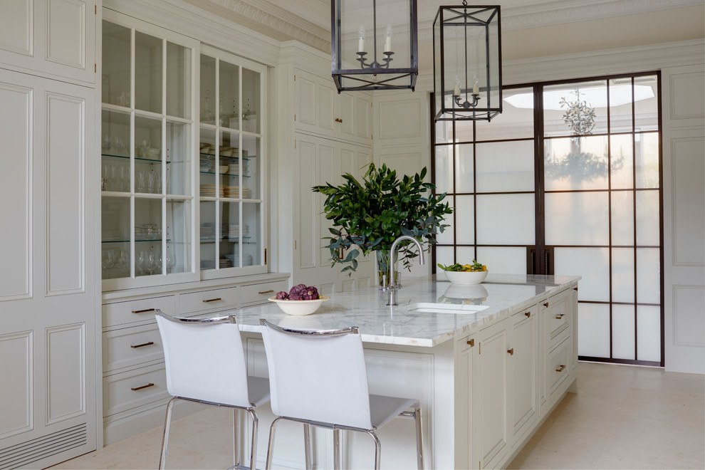 Large elegant galley limestone floor and beige floor eat-in kitchen photo in London with a double-bowl sink, recessed-panel cabinets, white cabinets, marble countertops, white backsplash, marble backsplash, white appliances, an island and white countertops