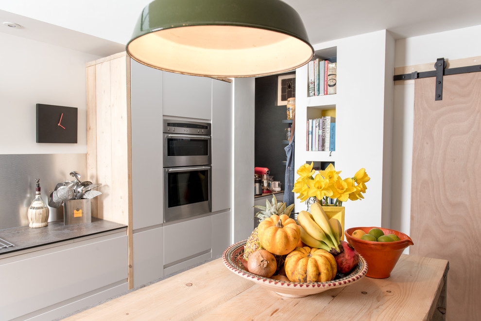 Photo of a small contemporary galley open plan kitchen in Devon with flat-panel cabinets, white cabinets, wood worktops, metallic splashback, stainless steel appliances, limestone flooring and an island.