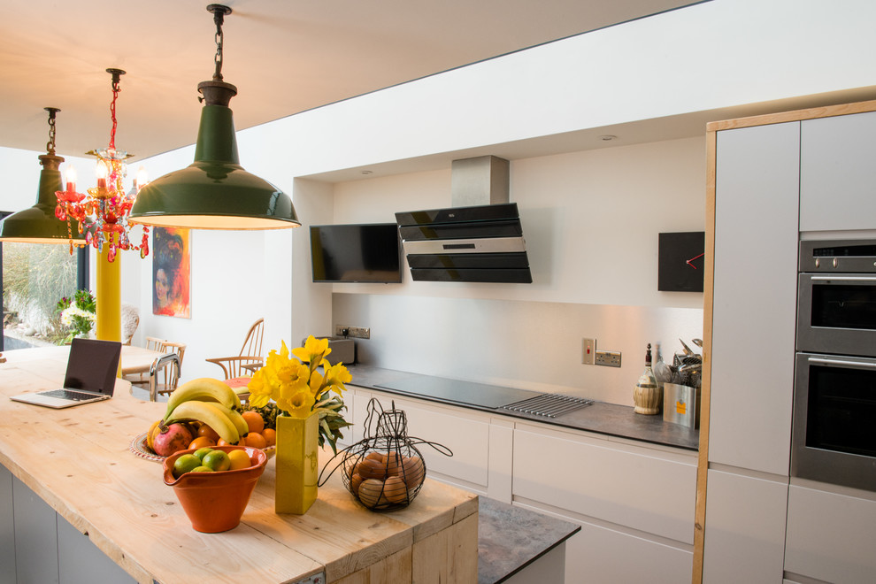 Design ideas for a medium sized contemporary galley open plan kitchen in Devon with flat-panel cabinets, white cabinets, wood worktops, metallic splashback, stainless steel appliances, limestone flooring, an island, metal splashback, beige floors and multicoloured worktops.