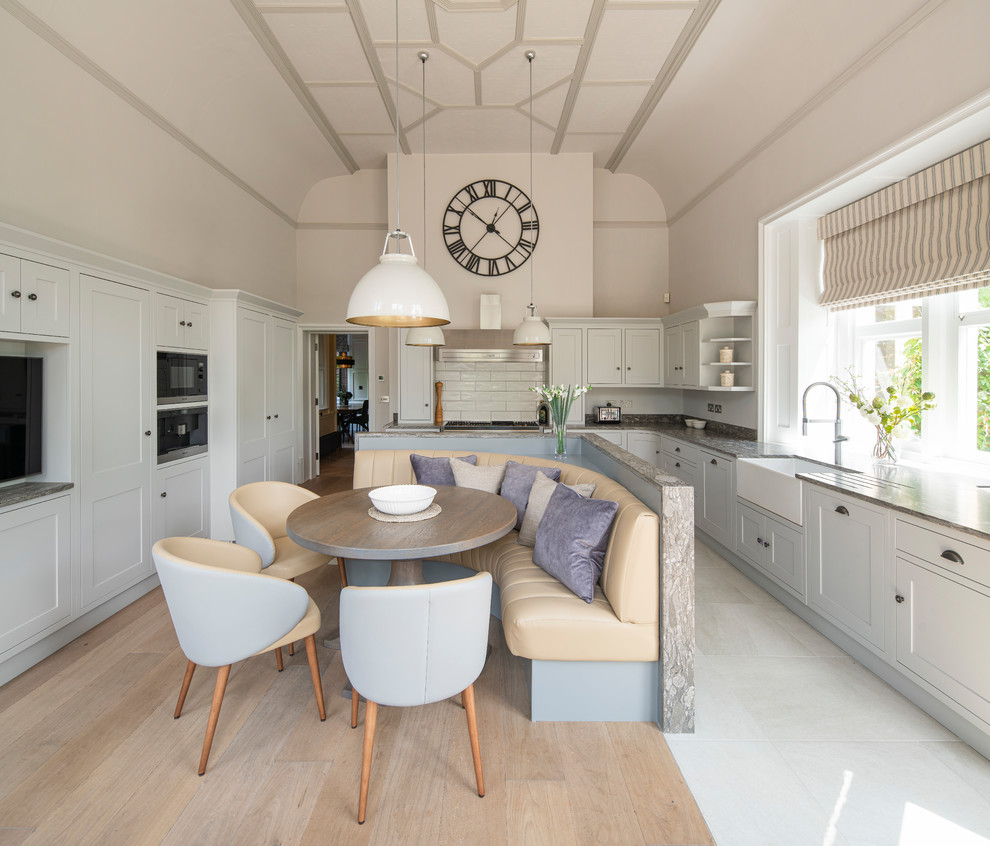 Design ideas for a farmhouse kitchen/diner in Surrey with a belfast sink, shaker cabinets, grey cabinets, granite worktops, white splashback, metro tiled splashback, stainless steel appliances and an island.