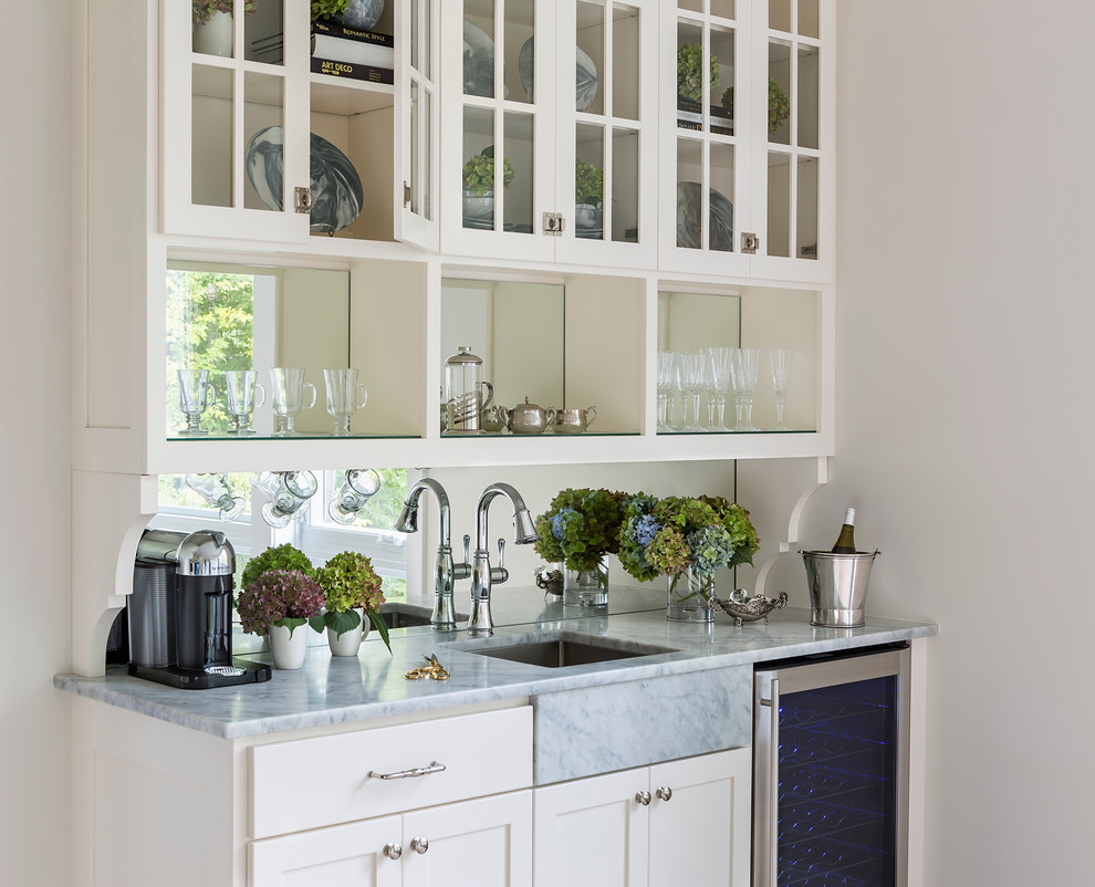 Idéer för ett mellanstort amerikanskt kök, med en undermonterad diskho, luckor med glaspanel, vita skåp, marmorbänkskiva, spegel som stänkskydd, ljust trägolv och en köksö