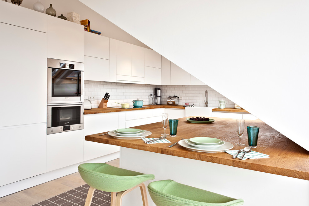 Exempel på ett stort modernt l-kök, med släta luckor, vita skåp, träbänkskiva, vitt stänkskydd, stänkskydd i tunnelbanekakel, rostfria vitvaror, ljust trägolv och en köksö