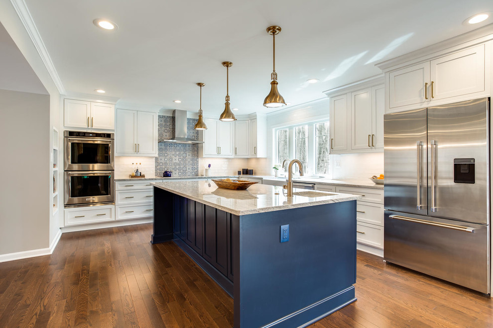 Classic l-shaped kitchen in DC Metro with a belfast sink, shaker cabinets, blue cabinets, white splashback, metro tiled splashback, stainless steel appliances, medium hardwood flooring, an island, brown floors and white worktops.