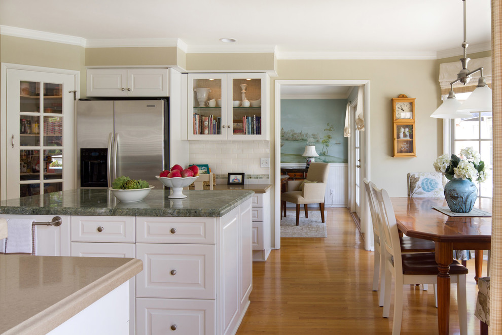 Inredning av ett klassiskt mellanstort kök, med luckor med upphöjd panel, vita skåp, marmorbänkskiva, vitt stänkskydd, stänkskydd i tunnelbanekakel, rostfria vitvaror, mellanmörkt trägolv och en köksö