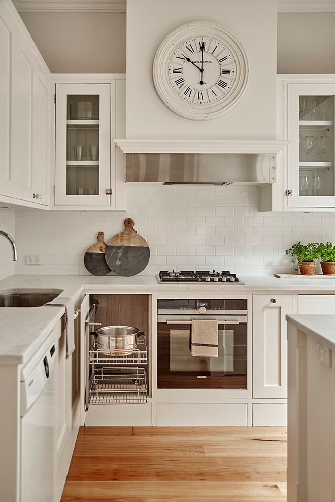 Bild på ett mellanstort lantligt kök, med en undermonterad diskho, vita skåp, marmorbänkskiva, vitt stänkskydd, rostfria vitvaror, ljust trägolv, en köksö, luckor med glaspanel och stänkskydd i tunnelbanekakel