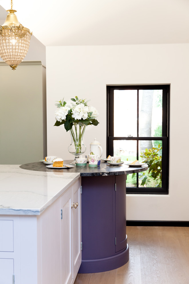 Cette photo montre une cuisine chic de taille moyenne avec un placard à porte shaker, des portes de placard blanches, un plan de travail en granite, parquet foncé, îlot et un sol marron.