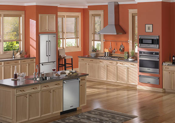 Klassische Wohnküche in U-Form mit Schrankfronten mit vertiefter Füllung, hellen Holzschränken, Küchenrückwand in Orange, Küchengeräten aus Edelstahl, hellem Holzboden und Kücheninsel in Jackson