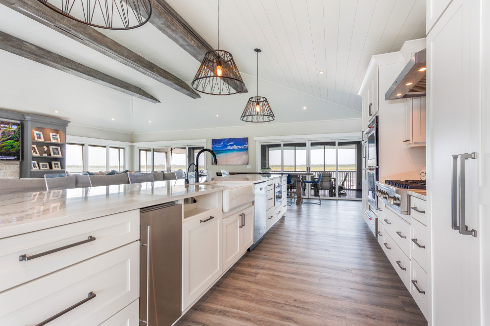 Example of a huge beach style single-wall vinyl floor, multicolored floor and exposed beam eat-in kitchen design in Jacksonville with a farmhouse sink, shaker cabinets, white cabinets, quartz countertops, black backsplash, glass sheet backsplash, stainless steel appliances, an island and multicolored countertops
