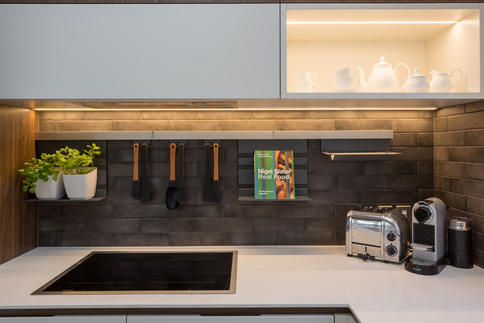 Photo of a medium sized contemporary u-shaped kitchen/diner in Auckland with white cabinets, composite countertops, brown splashback, porcelain splashback, black appliances, medium hardwood flooring, no island, a submerged sink, flat-panel cabinets and beige floors.