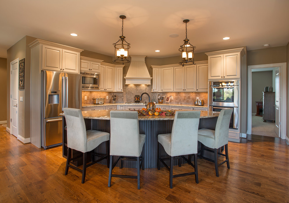 Example of a mid-sized transitional l-shaped medium tone wood floor eat-in kitchen design in Cincinnati with a drop-in sink, raised-panel cabinets, beige cabinets, granite countertops, beige backsplash, ceramic backsplash, stainless steel appliances and an island