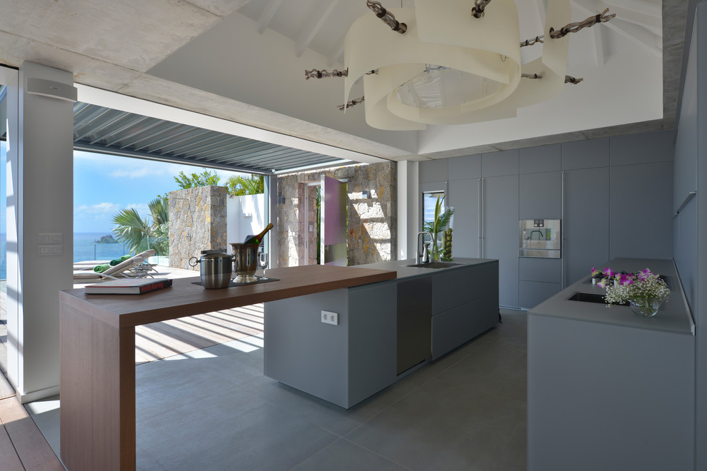 Стильный дизайн: параллельная кухня в морском стиле с врезной мойкой, плоскими фасадами, серыми фасадами, столешницей из акрилового камня, техникой из нержавеющей стали, бетонным полом и островом - последний тренд