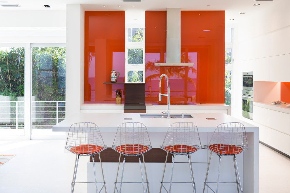 Contemporary kitchen in Other with a submerged sink, flat-panel cabinets, white cabinets, red splashback, glass sheet splashback, stainless steel appliances, an island, white floors and white worktops.