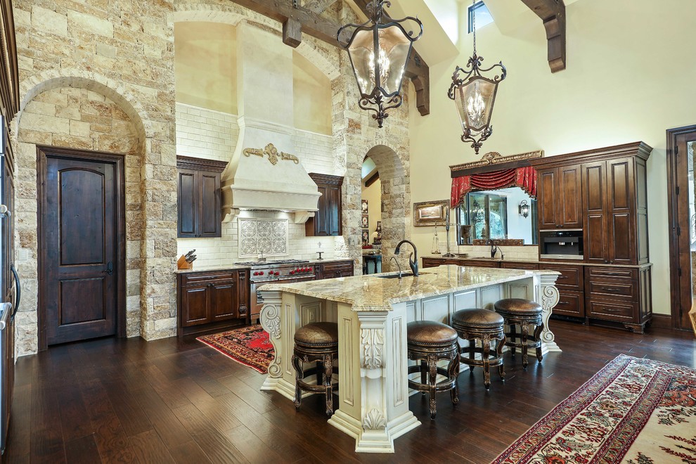Tuscan dark wood floor and brown floor kitchen photo in Austin with an undermount sink, raised-panel cabinets, dark wood cabinets, subway tile backsplash, stainless steel appliances, an island, white backsplash and multicolored countertops