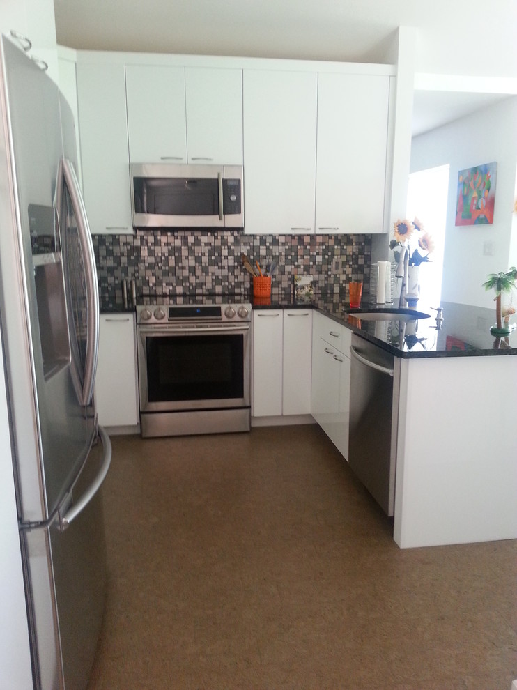 Foto på ett litet funkis kök, med en undermonterad diskho, släta luckor, vita skåp, granitbänkskiva, flerfärgad stänkskydd, stänkskydd i mosaik, rostfria vitvaror, korkgolv och en halv köksö