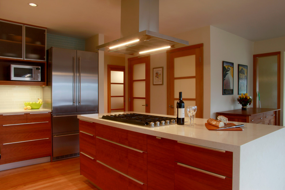 Exempel på ett mellanstort modernt kök, med en dubbel diskho, luckor med glaspanel, skåp i mellenmörkt trä, bänkskiva i kvarts, blått stänkskydd, stänkskydd i glaskakel, rostfria vitvaror, mellanmörkt trägolv och en köksö