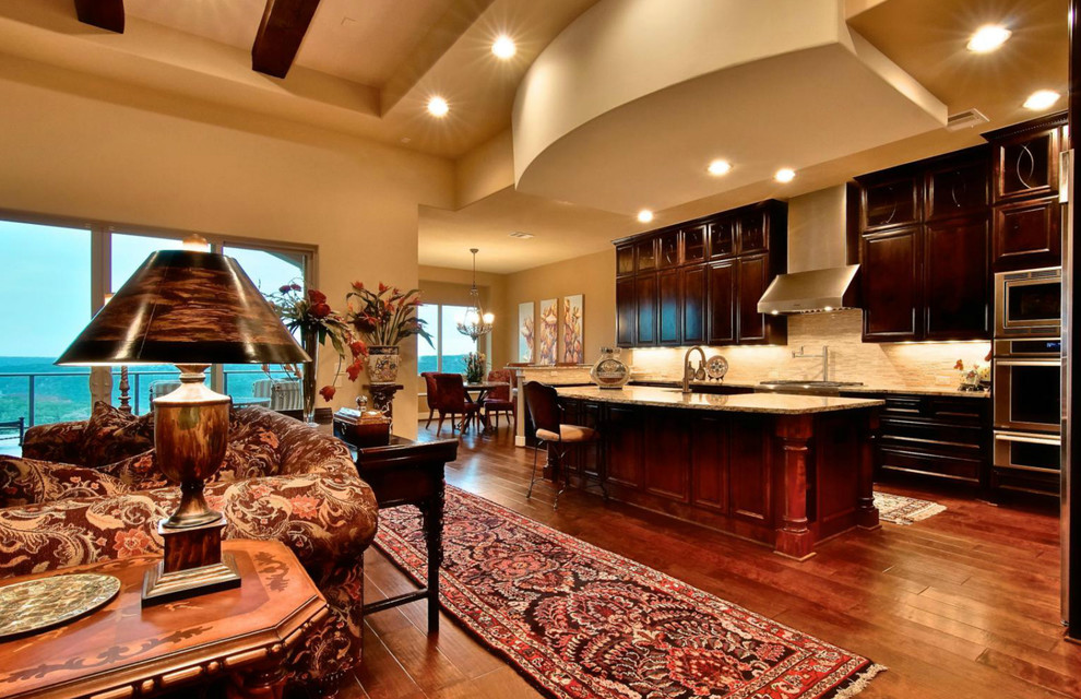 This is an example of a large mediterranean single-wall open plan kitchen in Austin with raised-panel cabinets, dark wood cabinets, beige splashback, stainless steel appliances, dark hardwood flooring and an island.