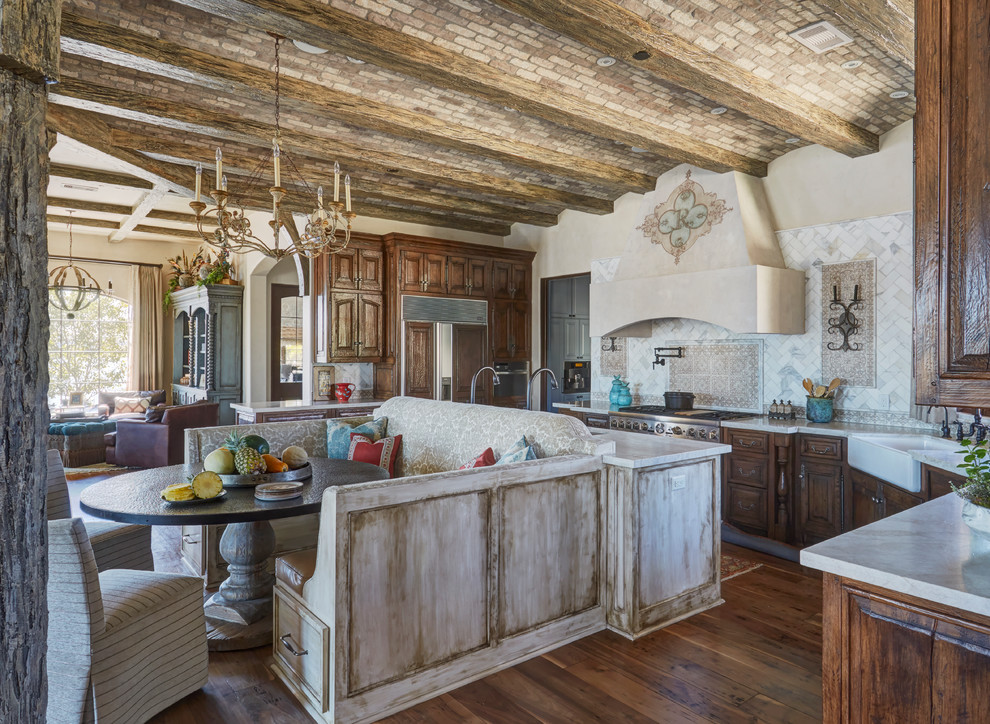 Exempel på ett medelhavsstil beige beige kök, med en rustik diskho, luckor med upphöjd panel, skåp i mörkt trä, vitt stänkskydd, rostfria vitvaror, mörkt trägolv, en köksö och brunt golv