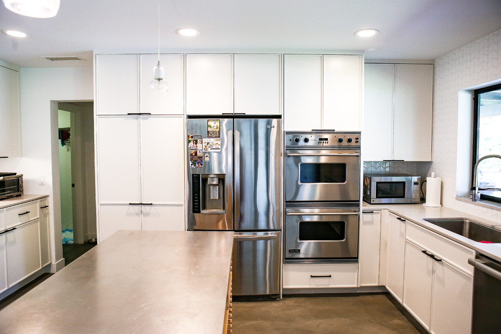 Photo of a medium sized modern u-shaped kitchen/diner in Orange County with a submerged sink, shaker cabinets, white cabinets, engineered stone countertops, white splashback, porcelain splashback, stainless steel appliances, concrete flooring, an island, grey floors and grey worktops.