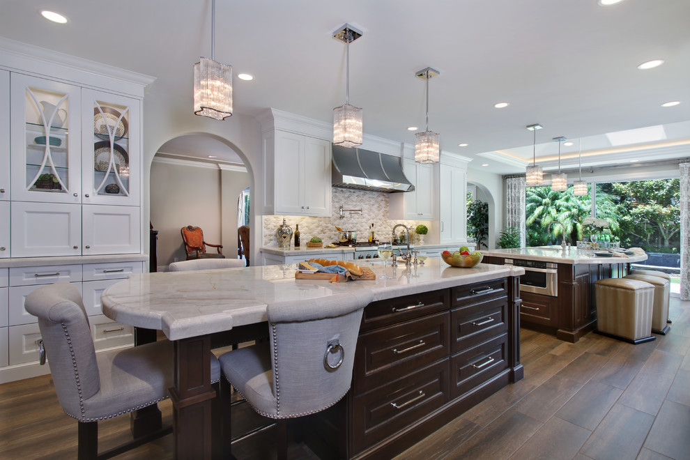 Design ideas for a large classic galley kitchen/diner in Orange County with multiple islands, a submerged sink, shaker cabinets, white cabinets, marble worktops, beige splashback, mosaic tiled splashback, stainless steel appliances and medium hardwood flooring.